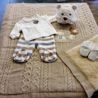 Ein weißer Pullover, eine gestreifte Hose für Kleinkinder und kleine Stoffschuhe werden auf einem Glastisch präsentiert