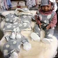 Eine Babypuppe trägt einen Mehrteiler mit Anzug, Jacke, Mütze, Schal und Schuhe in der Farbe Grau mit weißen Punkten